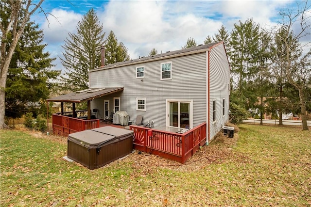 back of property featuring a wooden deck, a lawn, and a hot tub