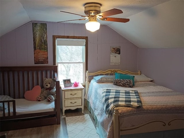 bedroom featuring wood walls, lofted ceiling, ceiling fan, light hardwood / wood-style floors, and a textured ceiling