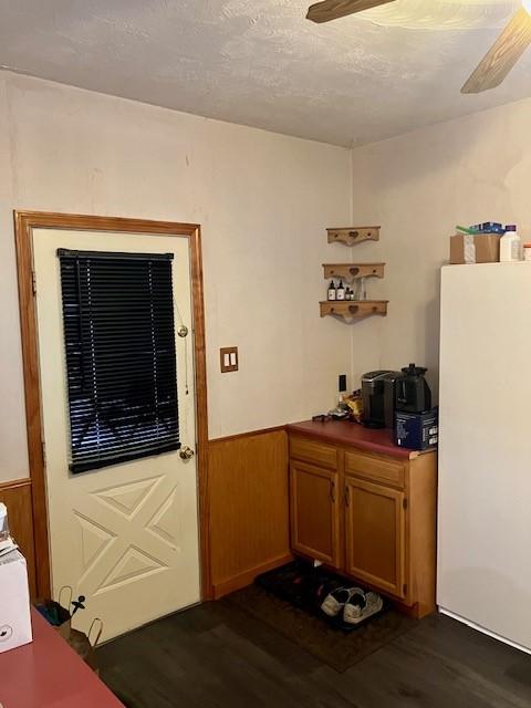 doorway to outside featuring a textured ceiling, dark wood-type flooring, wooden walls, and ceiling fan