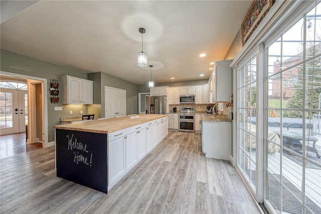 kitchen featuring sink, wooden counters, stainless steel appliances, white cabinets, and decorative light fixtures