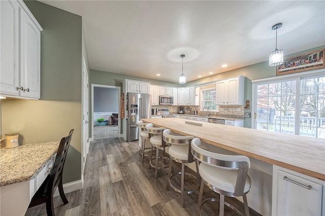 kitchen with appliances with stainless steel finishes, pendant lighting, tasteful backsplash, white cabinetry, and butcher block counters