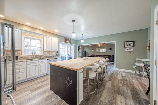 kitchen featuring sink, butcher block counters, white cabinets, decorative light fixtures, and stainless steel dishwasher