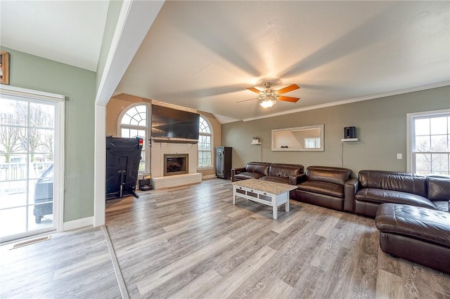 living room featuring vaulted ceiling, a large fireplace, hardwood / wood-style flooring, ceiling fan, and crown molding