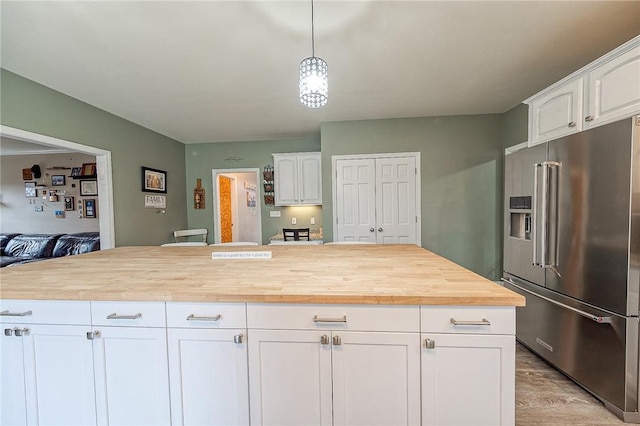 kitchen featuring decorative light fixtures, high end refrigerator, wooden counters, white cabinets, and a center island