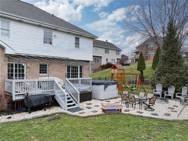 back of property with a patio area, a hot tub, a deck, a playground, and a fire pit