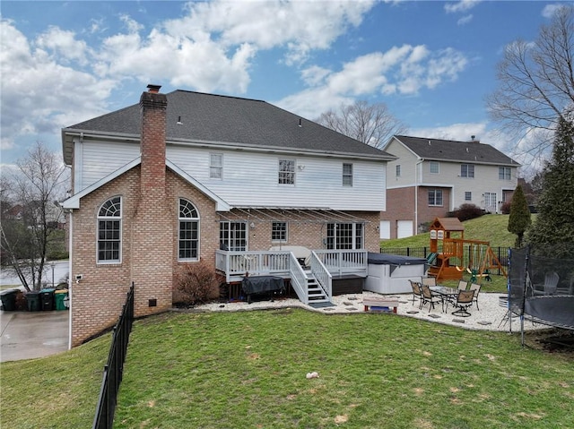 rear view of property with a playground, a deck, a trampoline, a yard, and a hot tub