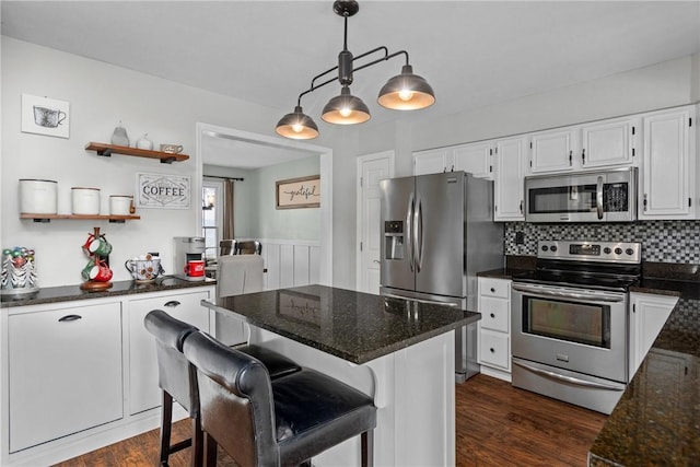 kitchen with appliances with stainless steel finishes, decorative light fixtures, white cabinets, dark hardwood / wood-style flooring, and a kitchen bar