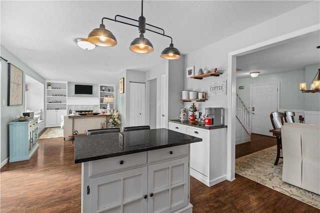 kitchen with dark hardwood / wood-style floors, decorative light fixtures, white cabinetry, dark stone counters, and a center island