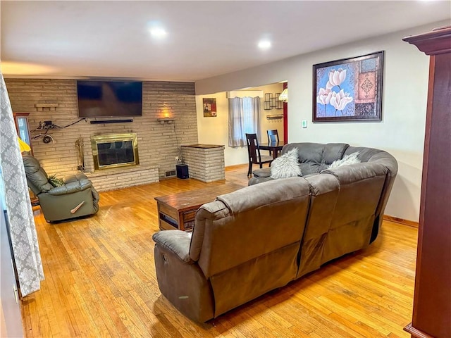 living room with brick wall, a brick fireplace, and light wood-type flooring