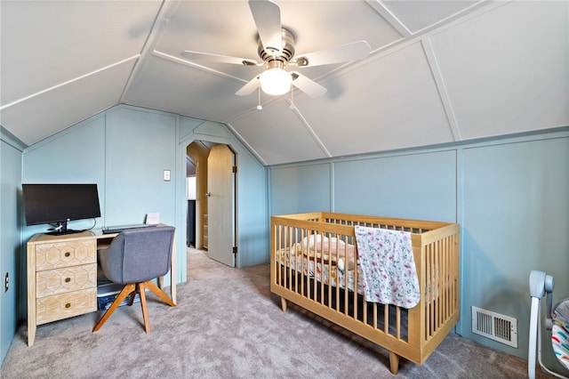 carpeted bedroom with a crib, lofted ceiling, and ceiling fan