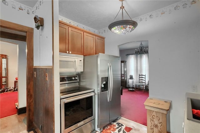 kitchen with appliances with stainless steel finishes, light carpet, an inviting chandelier, and decorative light fixtures