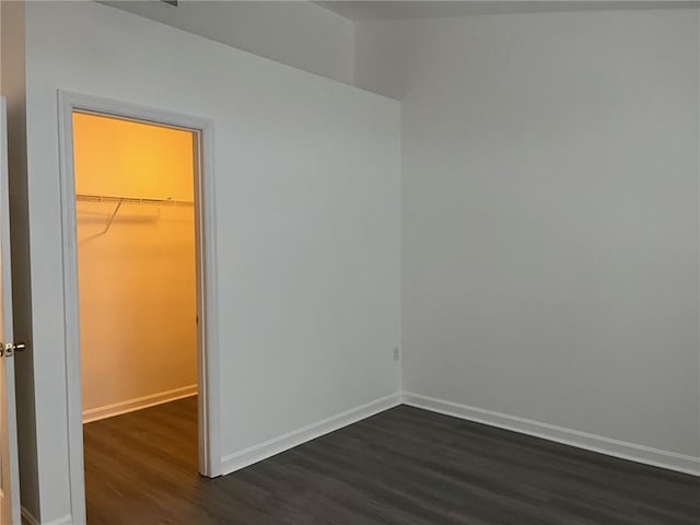 unfurnished bedroom with a spacious closet, dark wood-type flooring, and a closet