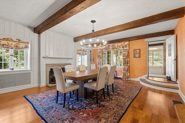 dining room featuring beamed ceiling, a wealth of natural light, a chandelier, and light hardwood / wood-style flooring