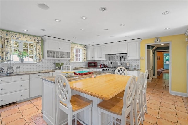 kitchen with white cabinets, dishwasher, custom range hood, a kitchen island, and backsplash