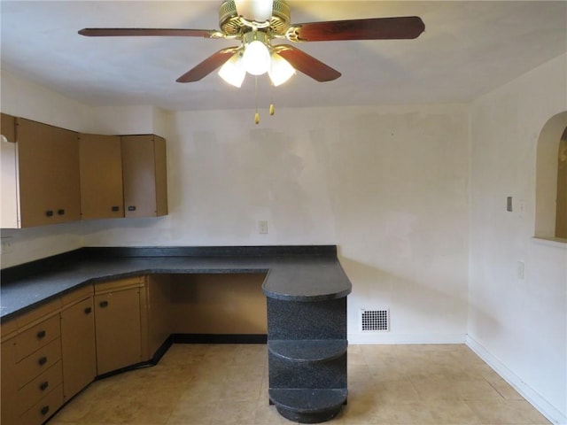 kitchen featuring baseboards, visible vents, arched walkways, built in study area, and dark countertops