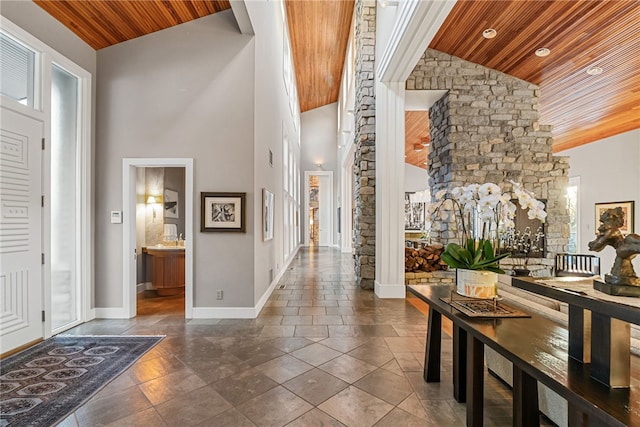 foyer entrance featuring high vaulted ceiling, decorative columns, wood ceiling, and baseboards