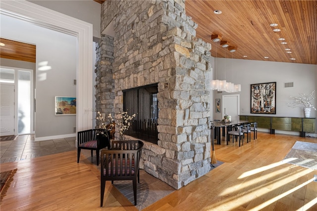 living area featuring wooden ceiling, high vaulted ceiling, wood finished floors, and a stone fireplace