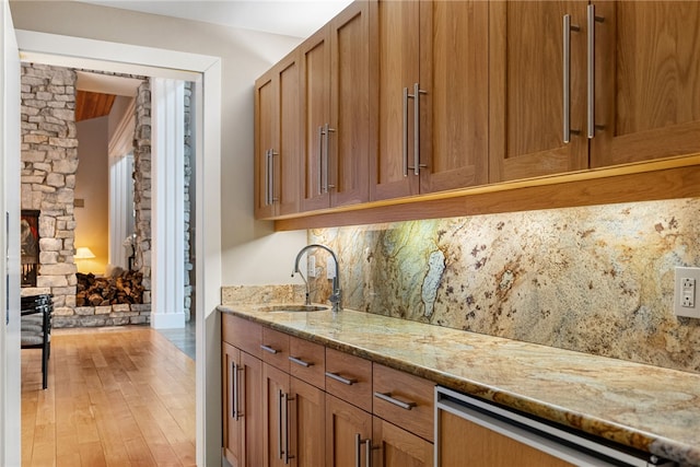 bar with dishwashing machine, light wood-style floors, a sink, and decorative backsplash