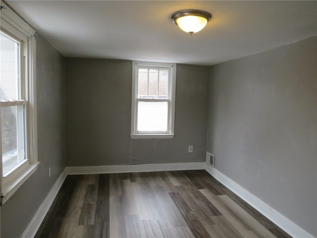 empty room featuring dark wood finished floors, visible vents, and baseboards