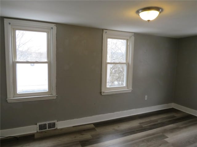 spare room with a healthy amount of sunlight, wood finished floors, visible vents, and baseboards