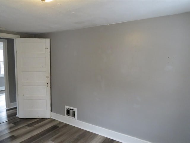 empty room featuring dark wood-style flooring, visible vents, and baseboards