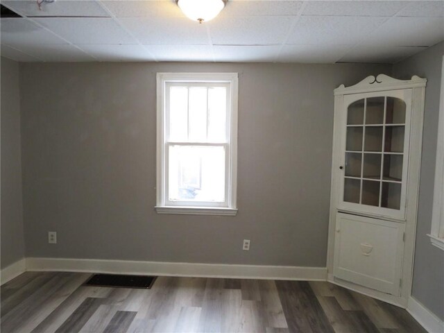 empty room with plenty of natural light, dark hardwood / wood-style floors, and a drop ceiling