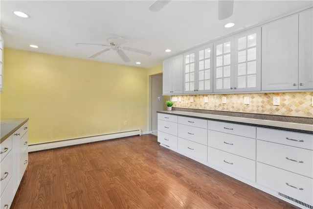 kitchen with white cabinetry, baseboard heating, hardwood / wood-style flooring, ceiling fan, and decorative backsplash