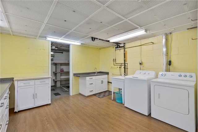 clothes washing area with cabinets, sink, washer and dryer, and light wood-type flooring