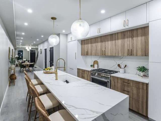 kitchen with sink, white cabinetry, high end range, a kitchen island with sink, and hanging light fixtures