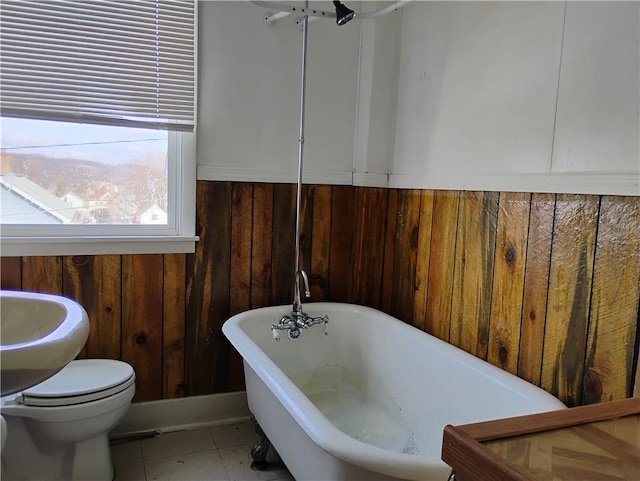 bathroom featuring tile patterned flooring, a washtub, wooden walls, and toilet