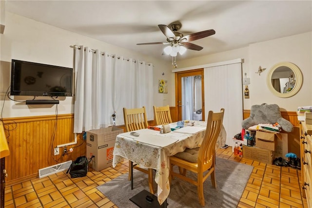 dining space with ceiling fan and wood walls