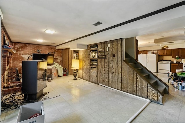 basement featuring a wood stove, wood walls, brick wall, and white refrigerator