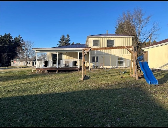 rear view of property with a wooden deck, a lawn, and a playground