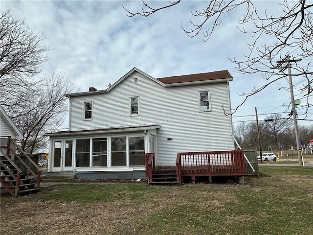 back of house featuring a sunroom, a deck, and a lawn