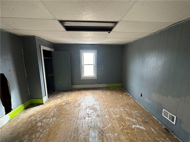 spare room with hardwood / wood-style flooring, a paneled ceiling, and wooden walls