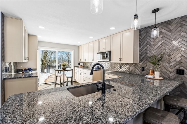 kitchen with sink, tasteful backsplash, decorative light fixtures, dark stone countertops, and kitchen peninsula