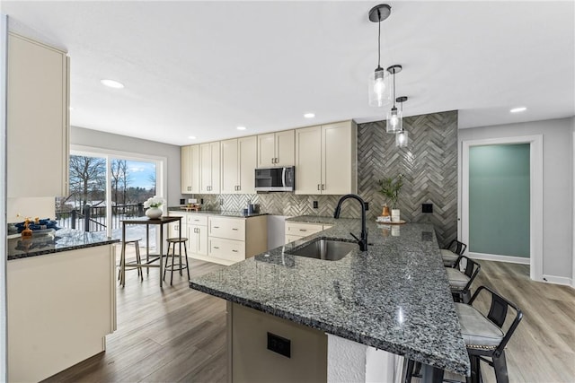 kitchen with a kitchen bar, sink, kitchen peninsula, pendant lighting, and dark stone counters