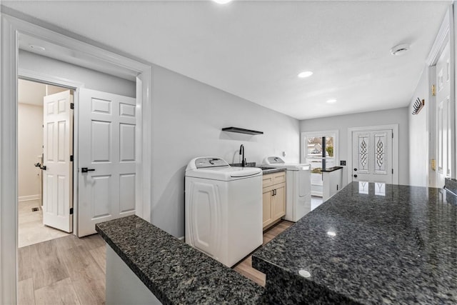 kitchen featuring white cabinetry, washer / clothes dryer, light hardwood / wood-style flooring, and dark stone counters