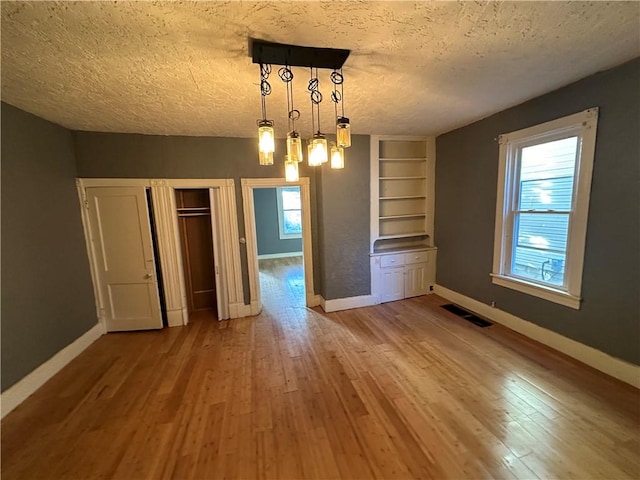 unfurnished dining area with built in features, wood-type flooring, and a textured ceiling