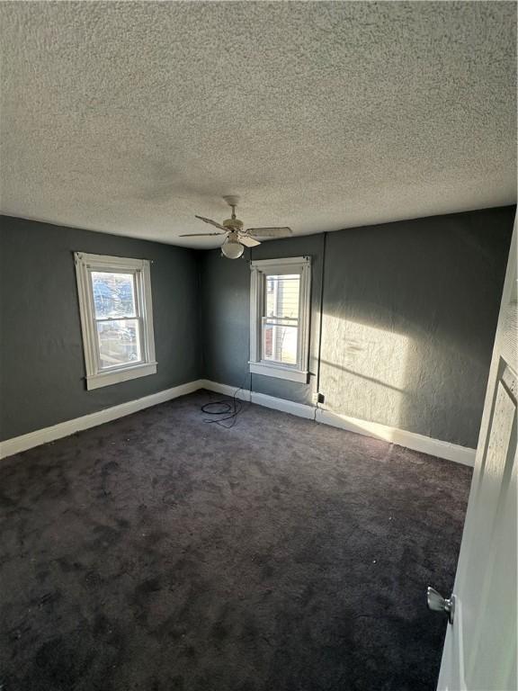 empty room featuring dark carpet, a textured ceiling, and ceiling fan