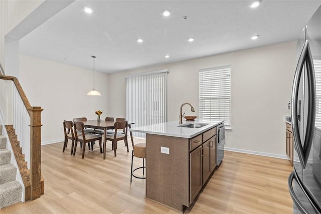 kitchen featuring pendant lighting, sink, fridge, a kitchen island with sink, and light wood-type flooring