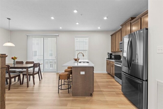 kitchen featuring a breakfast bar, sink, appliances with stainless steel finishes, pendant lighting, and a kitchen island with sink