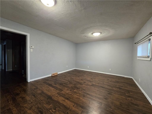 empty room with dark hardwood / wood-style flooring and a textured ceiling