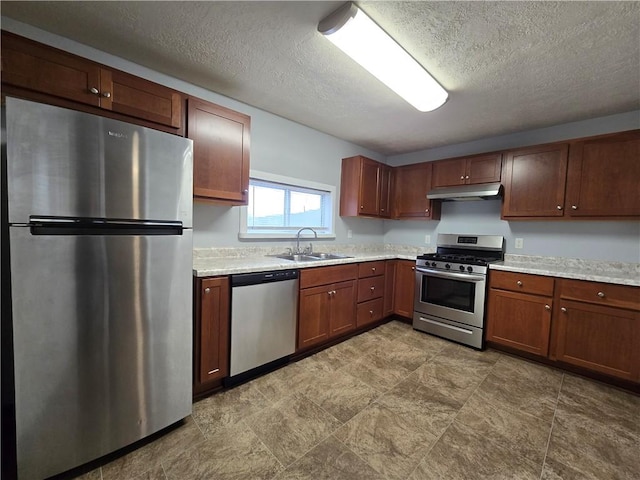 kitchen with appliances with stainless steel finishes, light stone countertops, sink, and a textured ceiling