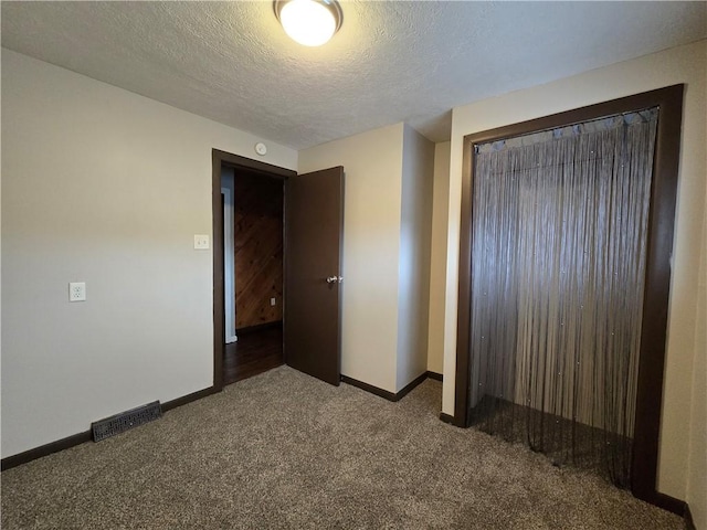 unfurnished bedroom with a textured ceiling, dark carpet, and a closet