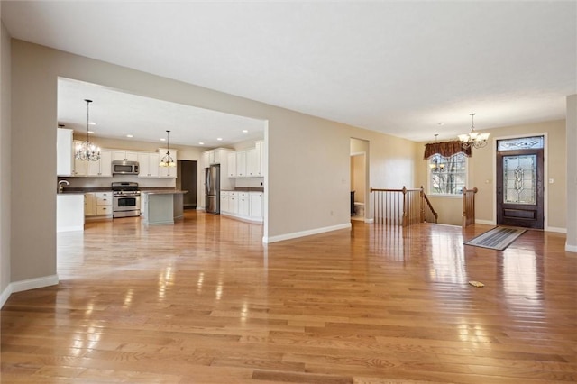 unfurnished living room with an inviting chandelier, sink, and light hardwood / wood-style floors