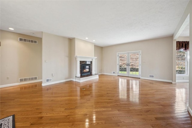 unfurnished living room with hardwood / wood-style floors, a wealth of natural light, a fireplace, and french doors