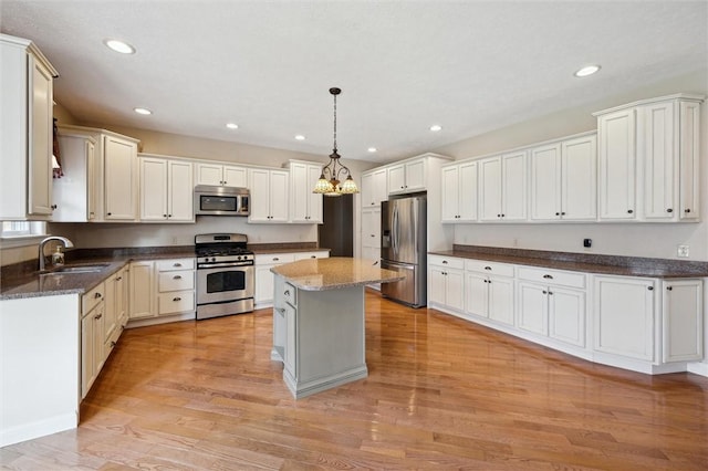 kitchen with pendant lighting, sink, appliances with stainless steel finishes, a center island, and light wood-type flooring