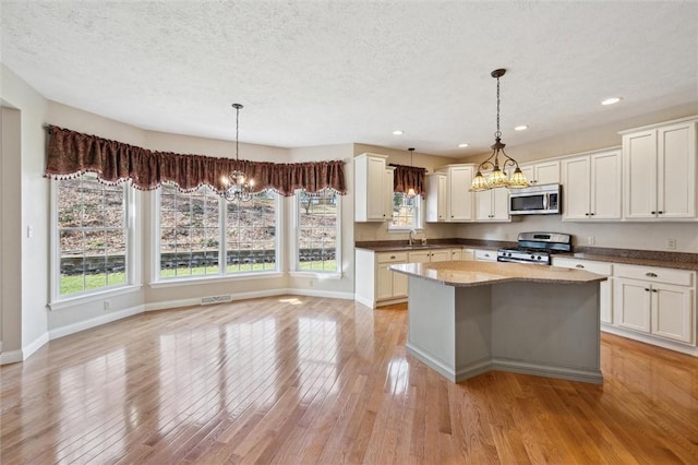 kitchen with appliances with stainless steel finishes, sink, pendant lighting, and an inviting chandelier