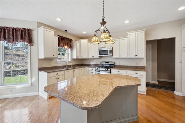 kitchen featuring appliances with stainless steel finishes, white cabinets, hanging light fixtures, a center island, and light wood-type flooring